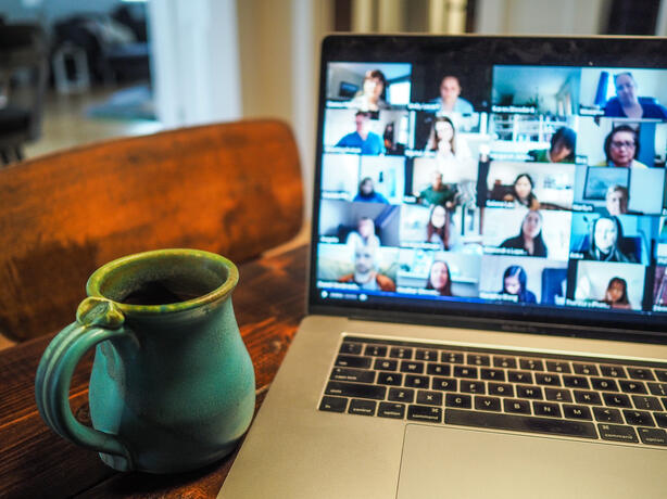 A lively zoom call on a laptop screen with a coffee cup beside it